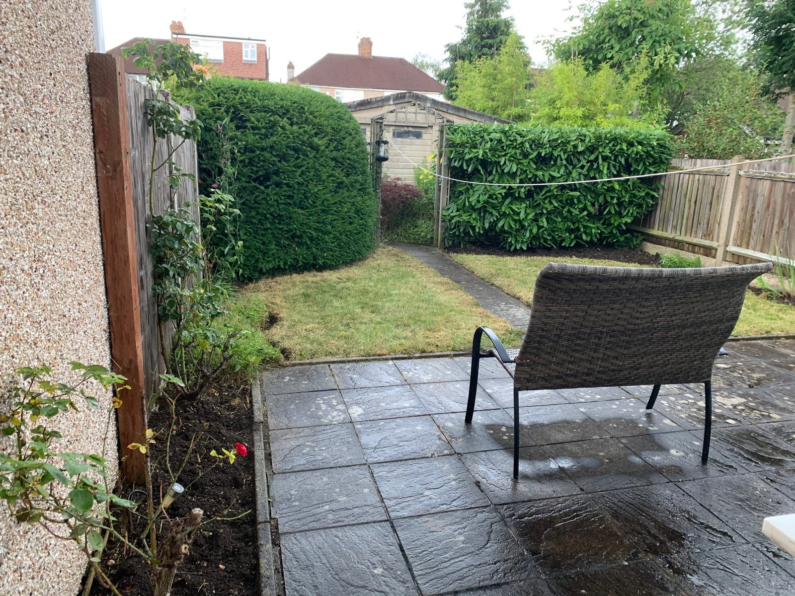 A lush, well-maintained garden featuring neatly trimmed emerald-green boxwood hedges, vibrant flower beds bursting with colorful roses, lavender, and salvias, and a pristine lawn with crisp edges. A winding stone pathway leads through the space, flanked by healthy shrubs and seasonal blooms under bright sunlight, showcasing professional garden maintenance at its finest.